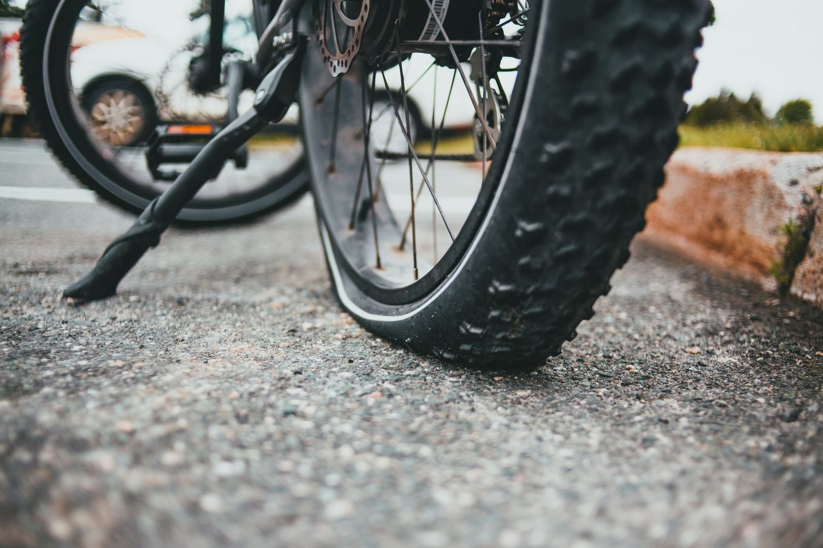 Close-up van een brede fietsband op grof asfalt naast een stoeprand